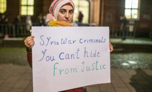 Syrian activist hold up poster saying Syria war criminals you can't hide from justice, Koblenz, January 2022